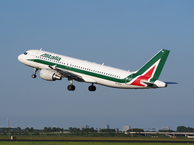 Ein Airbus A320-232 ERJ-EJZ der Alitalia startet vom Frankfurter Flughafen mit grünem Gras darunter, Bäumen und Gebäuden im Hintergrund und einem klaren blauen Himmel.