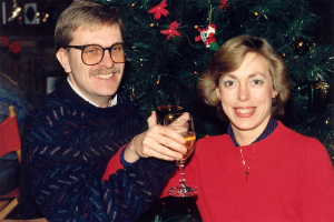 Ein Paar lächelt, waehrend es Gläser Wein hält, mit einem Weihnachtsbaum im Hintergrund.