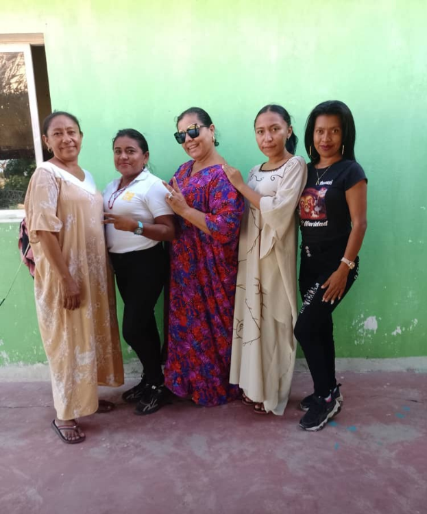 Gruppe von Frauen, die vor einer grünen Wand mit einem Fenster auf der linken Seite stehen und an einem Internationalen Frauentag teilnehmen.