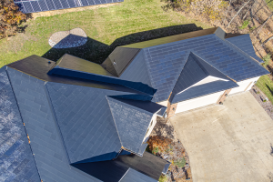 Ein Haus mit Solarmodulen auf dem Dach, umgeben von Bäumen, Gras und einem Zaun, aus der Vogelperspektive.