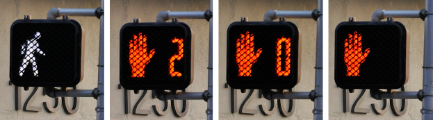 Eine an einem Gebäude angebrachte Ampel, die drei verschiedene Arten von Verkehrszeichen anzeigt.