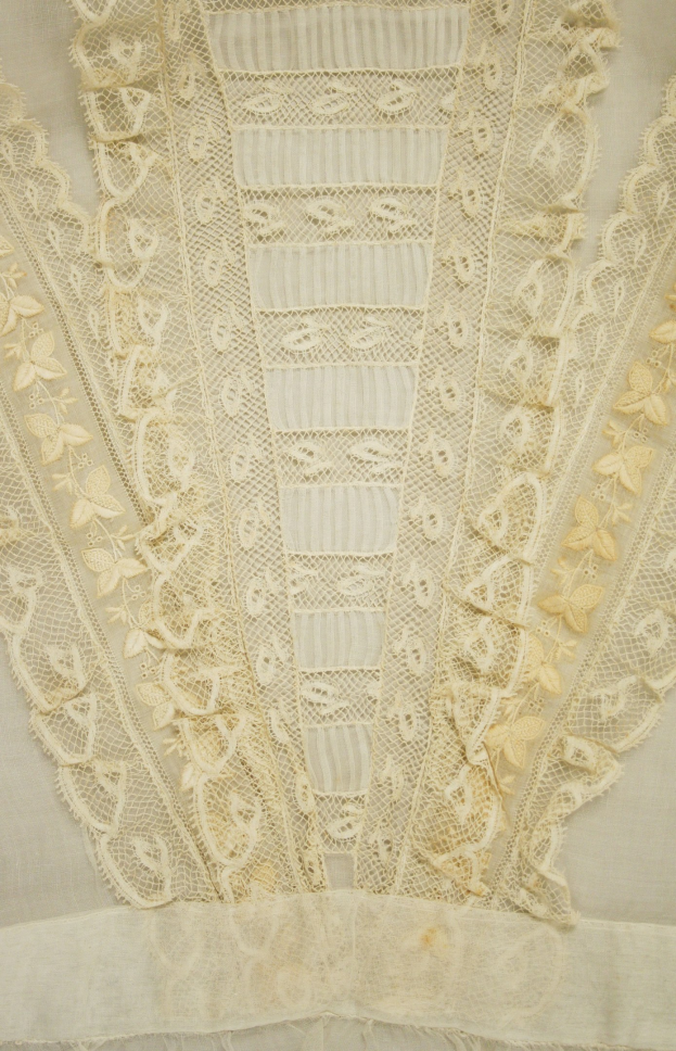 Nahaufnahme eines weißen Kleides mit aufwendiger Spitzenverzierung, das feine Muster und einen leichten, luftigen Stoff für den Sommer bietet.