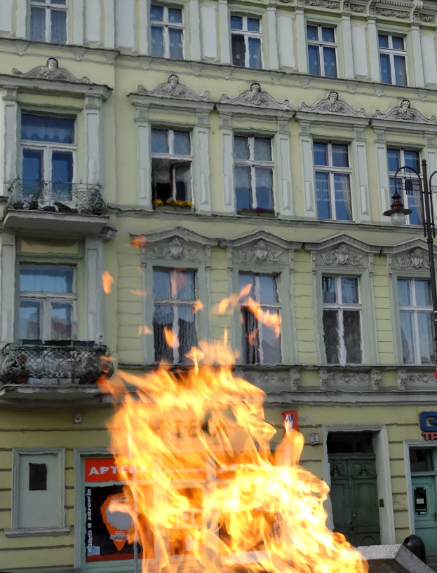 Ein großes Feuer brennt vor einem Gebäude mit Fenstern, Türen, einem Lichtmast und einer Tafel mit Schrift darauf.