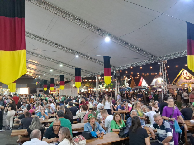 Große Gruppe von Menschen an Tischen unter einem Zelt beim Oktoberfest in München, Deutschland, mit festlicher Dekoration und Taschen auf den Tischen.