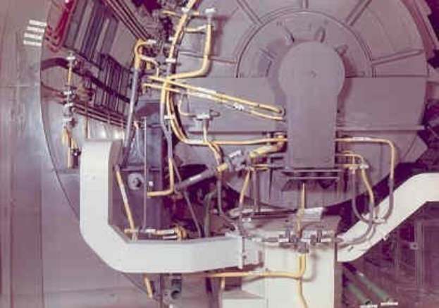 Großes industrielles Beschleunigergerät mit mehreren angeschlossenen Komponenten und Kabeln innerhalb eines Gebäudes.