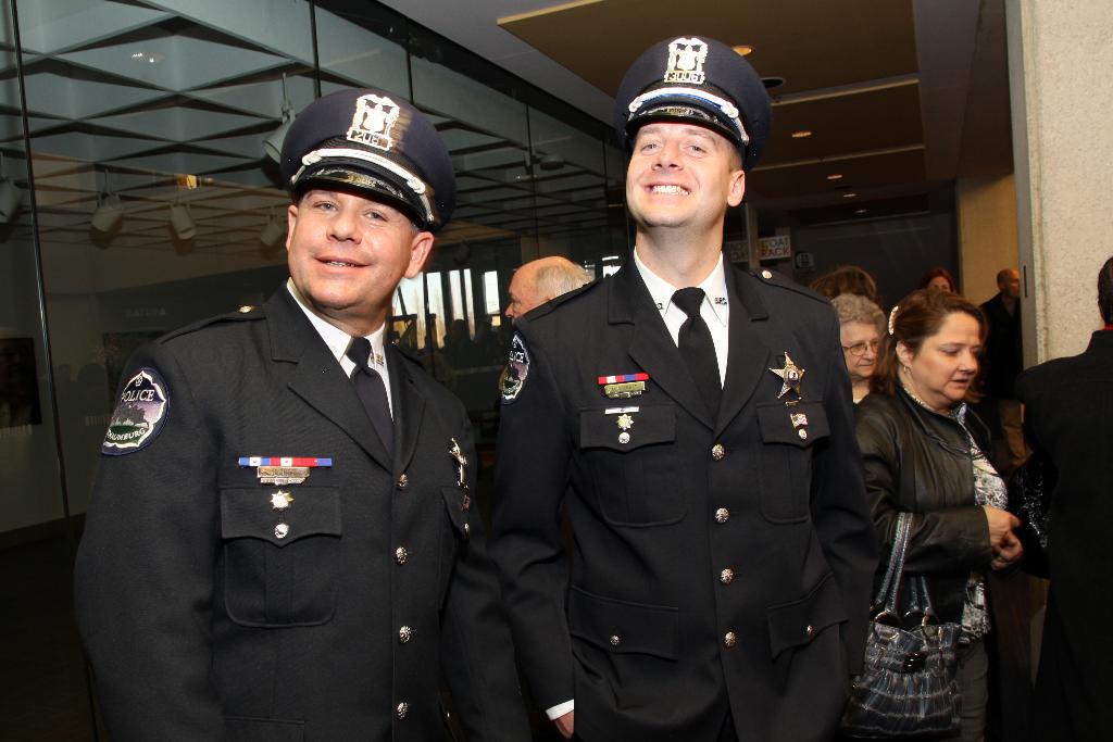 Zwei lächelnde Beamte vorne, Menschen in der Mitte, Glasfenster links, Lampen und Decke oben, Säulen und Menschen rechts.