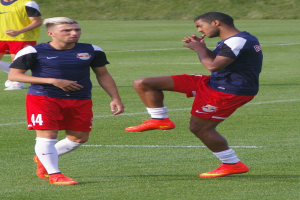 Zwei Männer in Fußballtrikots stehen auf einem Fußballfeld mit saftigem Gras.