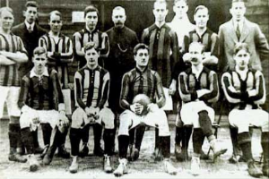 Ein Schwarz-Weiß-Foto einer Fußballmannschaft, einige stehen, einige sitzen, vor einer Wand mit dem Text "Ballymena Football Club" unten.