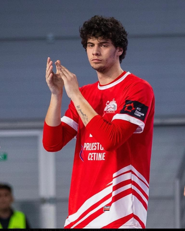 Ein Mann in rot-weißem Hemd, der im Vordergrund klatscht, mit einer weiteren Person und einer Wand im Hintergrund, und Text unten lesend "Copenhagen Futsal Club - Foto 1".