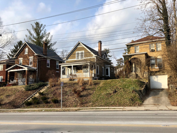Reihe von Häusern entlang einer Straße mit Fenstern, Türen, Säulen, Geländern, Stufen, Pflanzen, Gras, Bäumen und einem Pfahl mit einem Schild, unter einem bewölkten Himmel, repräsentiert eines der teuersten Häuser zum Verkauf in Detroit.