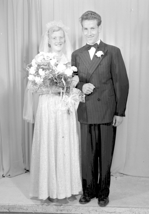 Ein Mann und eine Frau stehen nebeneinander auf einer Bühne, lächeln und die Frau hält einen Blumenstrauß, mit einem Vorhang dahinter.