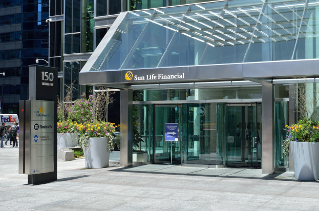 Moderner Glaswand-Sun Life Financial-Gebäude in Toronto mit einer Anzeigetafel, Blumentöpfen mit Blumen, Passanten, einer Straßenlaterne, einer Anzeigetafel, Fahrzeugen auf der Straße und einem bewölkten Himmel.