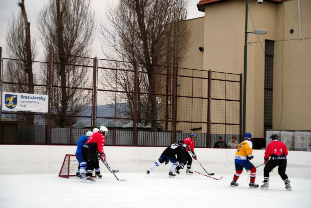 Menschen spielen Eishockey auf einem Eis mit Gebäuden, Bäumen und einer Straßenlaterne im Hintergrund.