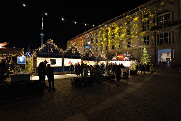Ein lebendiger Weihnachtsmarkt in Berlin, Deutschland, mit Menschen um beleuchtete Stände, festliche Décor und Fenster mit Lichtern unter einem dunklen Himmel.