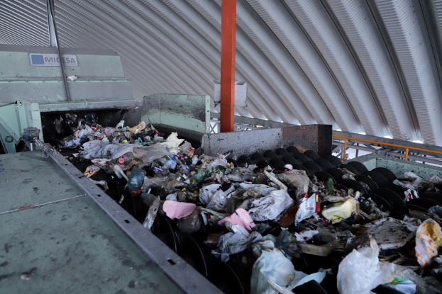 Großer Müllberg auf einem Förderband in einer Recyclinganlage mit Maschine und Metall Dach.