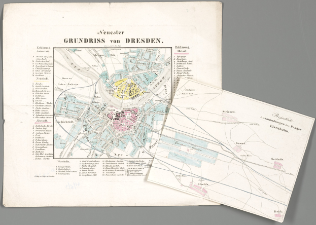 Alte Karte von Dresden, Deutschland, mit detaillierten Straßen, Gebäuden und Sehenswürdigkeiten, begleitet von zwei Papieren im Vordergrund vor einem grauen Hintergrund.