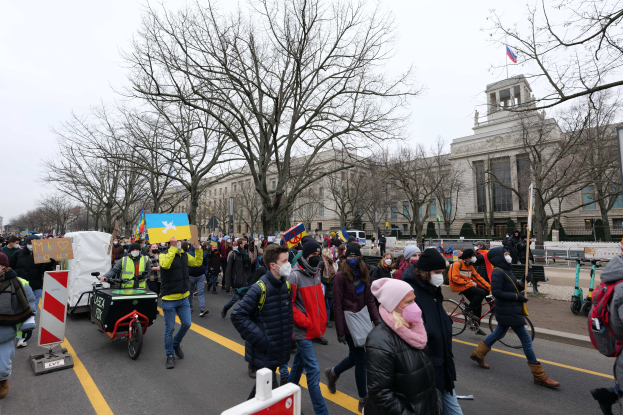 Eine große Gruppe von Menschen marschiert auf einer Stadtstraße, einige halten Schilder und andere fahren Fahrräder, mit Bäumen und einem Gebäude im Hintergrund bei klarem blauem Himmel in Washington, D.C. am 21. Januar 2020.
