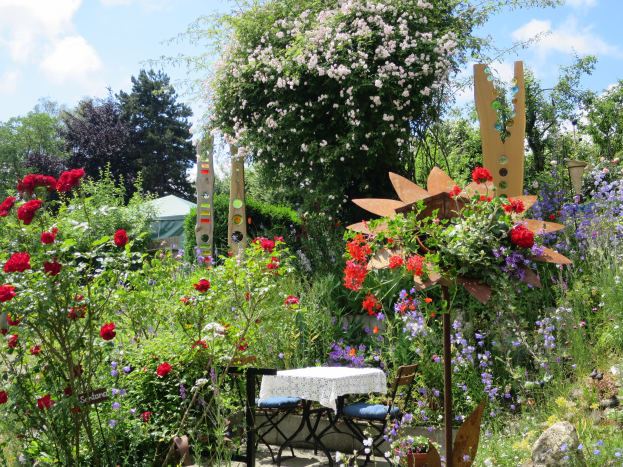 Ein Garten voller bunter Blumen und Pflanzen, mit einem Tisch und Stühlen in der Mitte, vor Bäumen und einem bewölkten Himmel auf der Chelsea Flower Show.