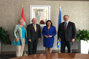 Eine Gruppe strahlender Menschen um einen Tisch mit Papieren herumstehend, umgeben von Fahnen, Topfpflanzen und einem Foto auf der Wand, die die Unterzeichnung eines Memorandums von Verständigung zwischen den Vereinigten Staaten und Kanada feiern.