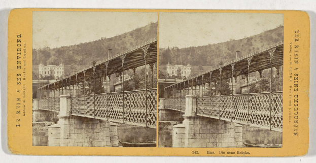 Schwarz-weißes Foto einer Brücke, die einen Fluss in Leipzig, Deutschland, überspannt, mit Gebäuden, Bäumen und einem Hügel im Hintergrund.