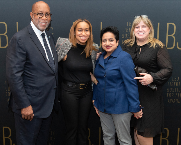Eine Gruppe von vier Personen, die auf einem roten Teppich stehen, lächeln und für ein Foto posieren, mit einem 'Liberty Justice for All Awards'-Schild im Hintergrund.