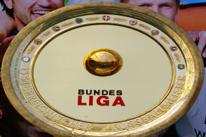Goldener Schild mit "Bundesliga"-Text in der Hand eines Mannes, Hintergrundbanner mit drei Personenbildern.