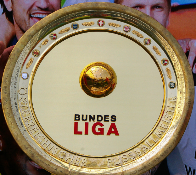 Goldener Schild mit "Bundesliga"-Text in der Hand eines Mannes, Hintergrundbanner mit drei Personenbildern.
