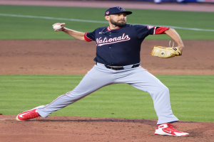 Ein Baseballspieler in einer Mütze und Handschuhen wirft auf einem Rasenfeld, mit Menschen und Texttafeln im Hintergrund, die einen World-Series-Sieg der Washington Nationals anzeigen.