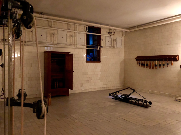 Ein unordentlicher Raum im ehemaligen Gefängnis St. Louis mit Seilen, Fitnessgeräten und anderem Equipment, einem Schrank, einem Fenster und einer Deckenlampe.