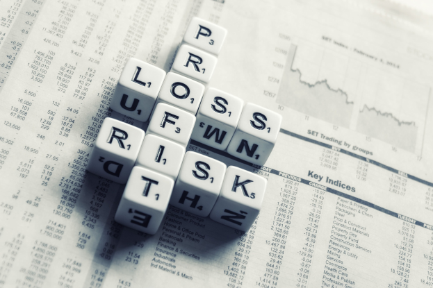 Kreuzworträtsel mit den Wörtern "Verlust, Risiko und Risiko" über einer Zeitung mit Text und Zahlen, das eine finanzielle Planung und Risikomanagement suggeriert.