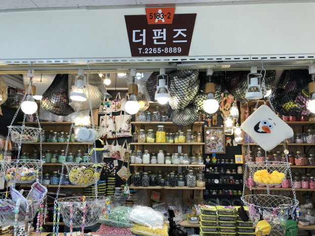Ein unordentlicher Laden in Seoul mit verschiedenen Gegenständen wie Körben, Lichtern, Flaschen und Spielzeugen auf Regalen, mit einer Tafel öber dem Eingang, die auf einen top-bewerteten koreanischen Shop hinweist.