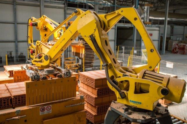 Industrielles Lager mit gestapelten Kisten, Kränen, Zaun, Pfosten und einer fernen Wand in einer Fertigungsanlage.