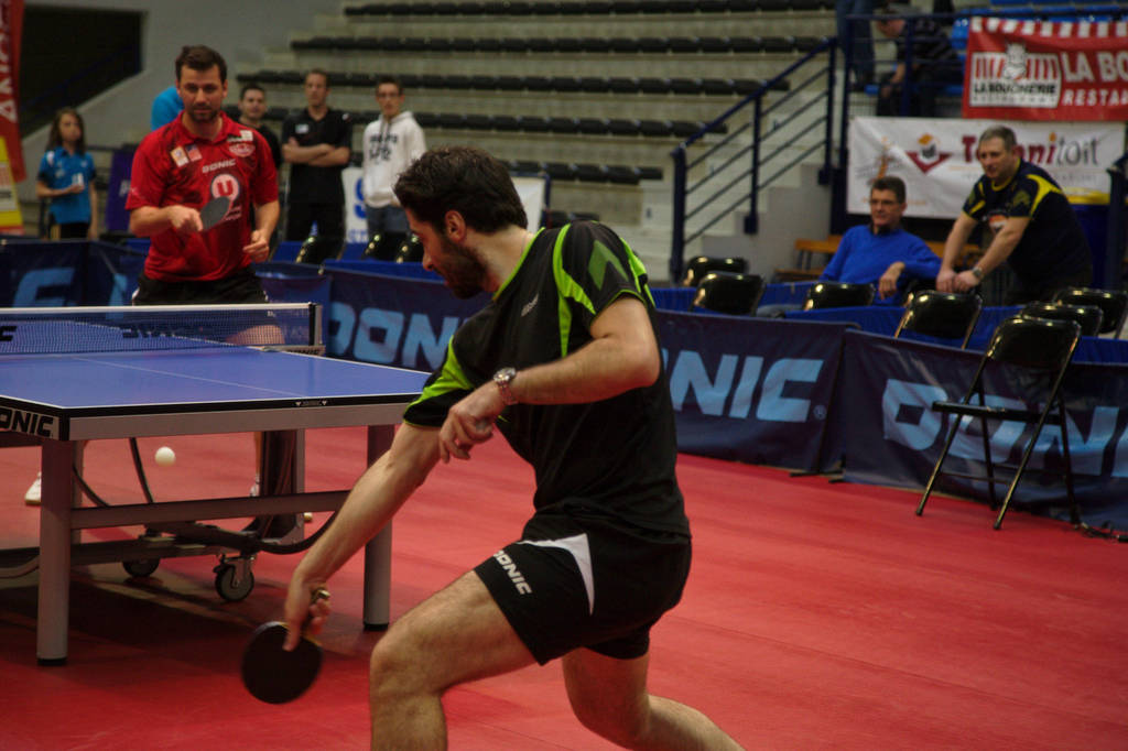 Eine Gruppe von Menschen in verschiedenen Farben, darunter schwarz, weiß und blau, sitzt um einen Tisch mit einem Spiel im Gange, mit Stühlen und einer Treppe im Hintergrund.
