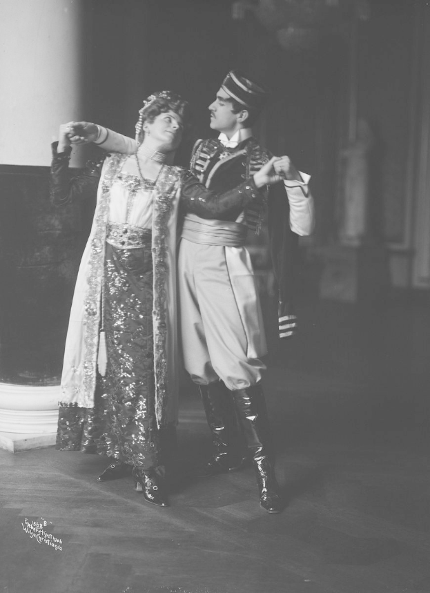 Schwarzes und weißes Foto eines Mannes und einer Frau, die in einem Ballsaal tanzen, mit einer Säule und einer Wand im Hintergrund; der Mann trägt Schuhe, was auf eine Vorstellung hinweist.