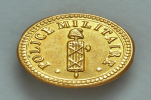 Eine Goldm├╝nze mit der Aufschrift "Police Militaire" vor einem wei├čem Hintergrund.
