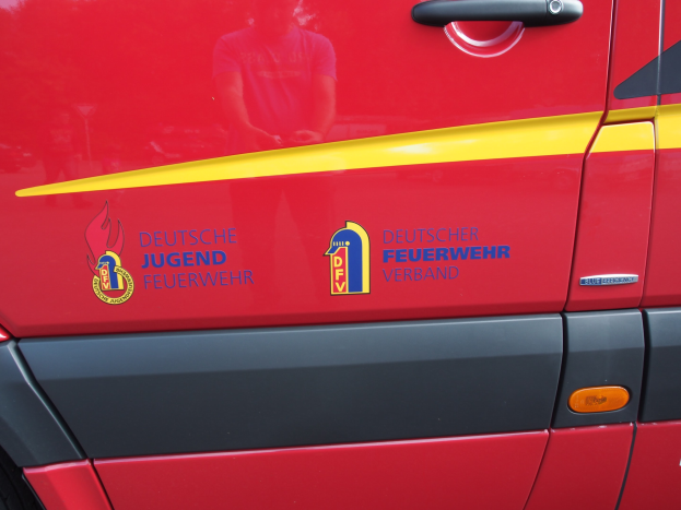 Roter Van mit einer gelben Streifen, Türgriff und einem Schild-Logo mit einem Löwen in einem Lorbeerkranz, beschriftet mit "Deutsche Jugendfeuerwehr Verband."