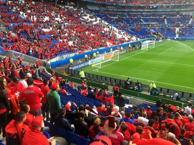 Eine große Menschenmenge in einem Stadion schaut einem Fußballspiel zu, mit Bannern, einem Torpfosten und Deckenbeleuchtung.
