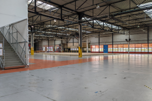 Ein großes industrielles Lagerhaus mit zahlreichen Fenstern, Metallstangen, einer Treppe mit Geländer, einem Schild, Deckenleuchten und zusätzlichen Stangen.