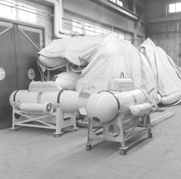 Ein Schwarz-Weiß-Foto eines Raums, der mit verschiedenen Tanktypen gefüllt ist, darunter eine Wasserstoffbombe, mit einer Wand, einer Tür, Fenstern, Rohren und anderen Gegenständen im Hintergrund.