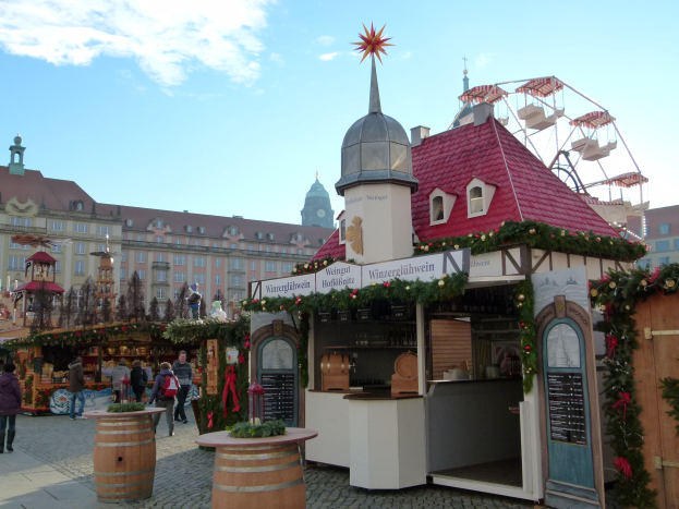 Ein geschäftiger Weihnachtsmarkt in Nürnberg, Deutschland mit Menschen um dekorierte Stände, einem Riesenrad im Hintergrund und einer Tafel mit Schrift auf der rechten Seite.