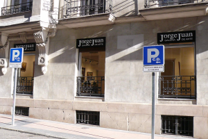 Ein mehrstöckiges Gebäude mit Fenstern, Geländern, Türen und Säulen, das Werbetafeln auf Pfählen entlang des Gehwegs und sichtbare Innenobjekte aufweist, die eine belebte Stadtkulisse suggerieren.