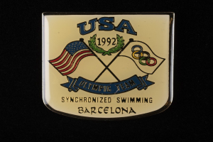 Abzeichen mit 'USA Olympic Team Synchronized Swimming Barcelona' Text, rote und blaue Flaggen auf schwarzem Hintergrund.
