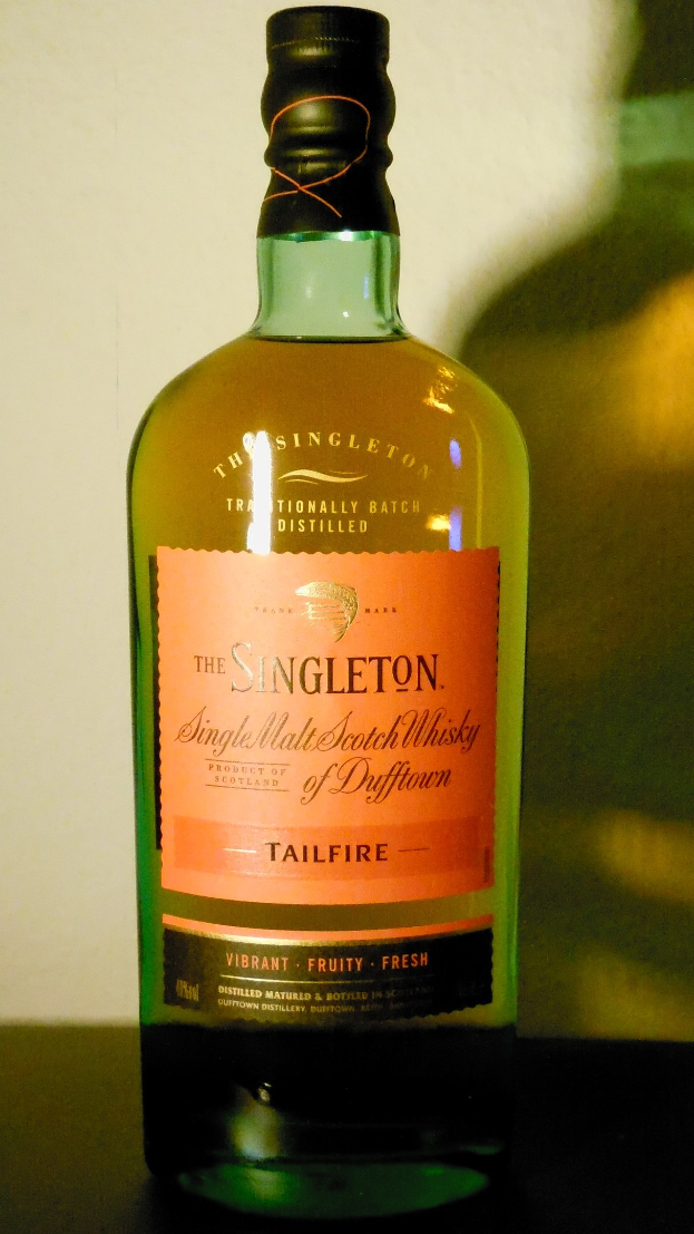 Eine tiefe bernsteinfarbene Flasche Singleton of Dufftown Tailfire Single Malt Scotch Whisky mit einem schwarzen Etikett, das ein Wappen mit einem Löwen und einer Burg zeigt.
