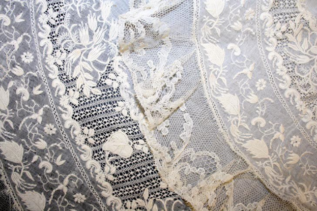 Nahaufnahme eines weißen Hochzeitskleids mit feiner, kunstvoller Spitzenverzierung mit verschiedenen Mustern auf einem leichten, luftigen Stoff.