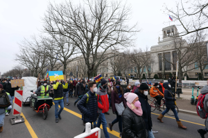 Eine große Gruppe von Menschen marschiert auf der Straße in Washington, D.C. am 21. Januar 2020 mit Schildern und Transparenten, einige fahren Fahrräder, Schildtafeln mit Stangen, Bäume und einen klaren blauen Himmel im Hintergrund.