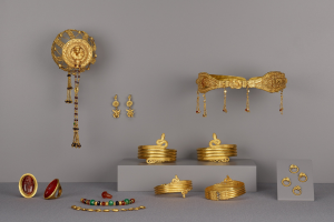 Goldschmuck-Display mit Armbändern, Ringen und anderen Stücken auf einer Oberfläche, mit zusätzlichen Stücken an der Wand im Hintergrund.