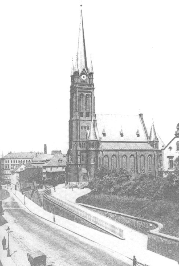 Schwarzes und weißes Foto einer Stadtstraße mit der St. Peter Kirche in Wiesbaden, Deutschland im Hintergrund, flankiert von Gebäuden, Bäumen, Fahrzeugen und Passanten.