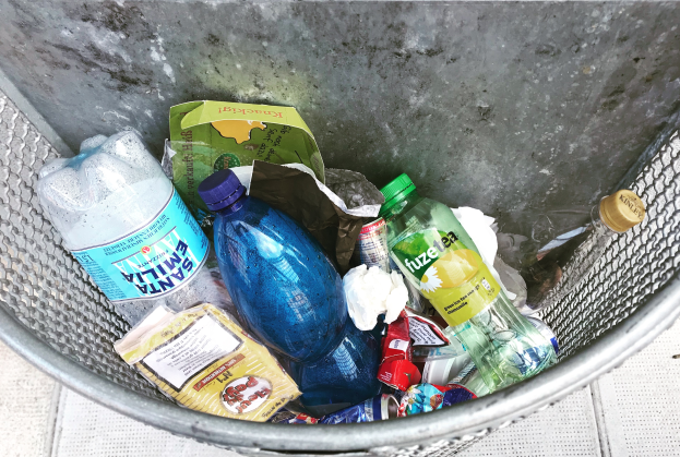 Ein Metallmüllcontainer gefüllt mit Plastikflaschen, Tüten und diversen anderen Gegenständen.