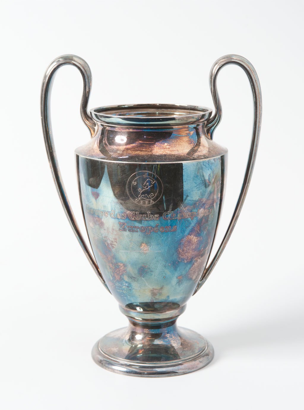 Ein stählerner UEFA Champions League Pokal mit zwei Griffen in Blau und Silber, der mit "UEFA Champions League" beschriftet ist, vor einem weißen Hintergrund dargestellt.