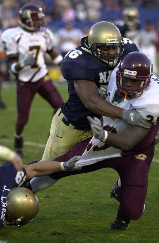 Zwei Fußballspieler in Helmen und Uniformen stoßen auf dem Feld zusammen, während andere zusehen.